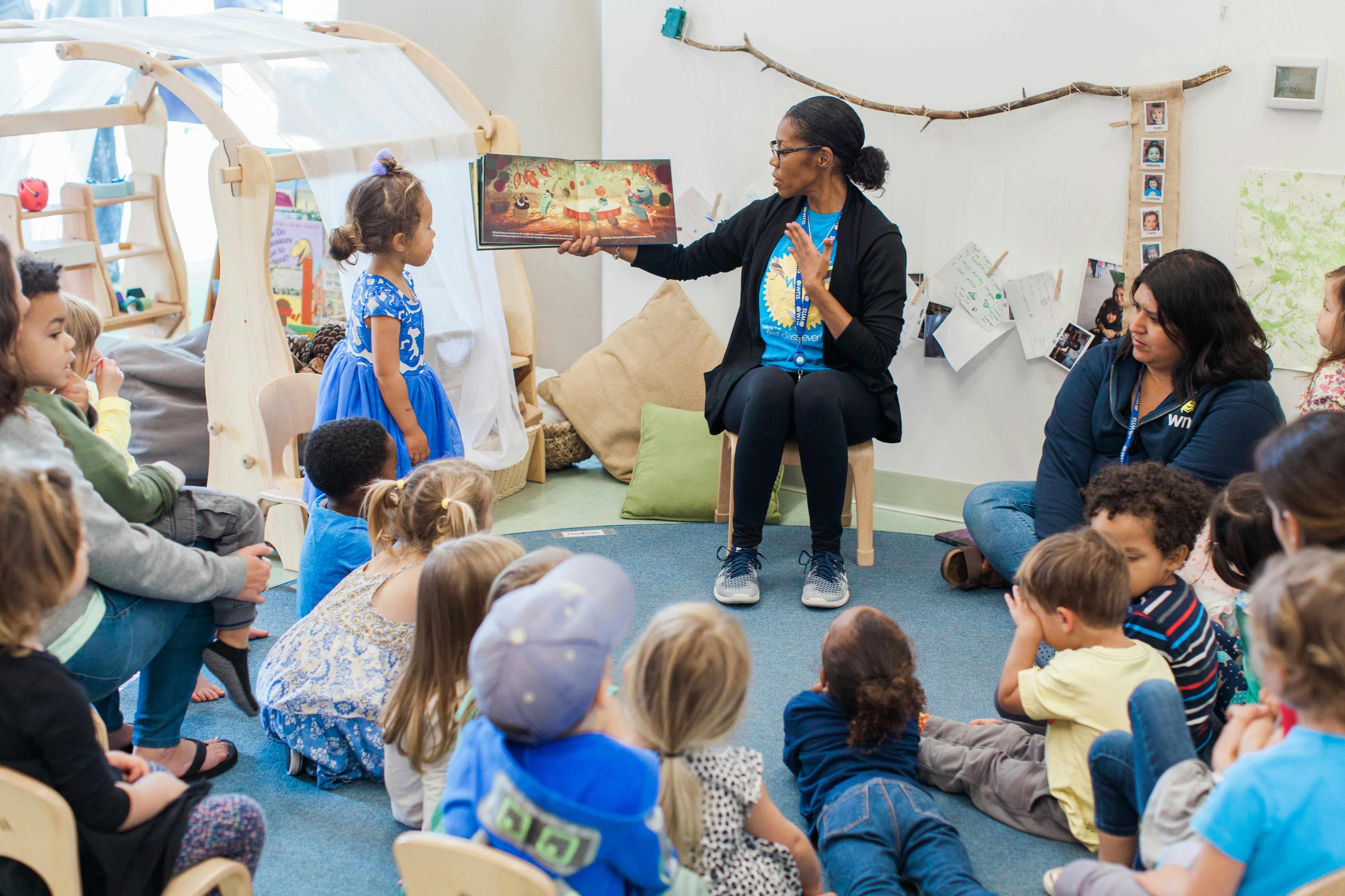 Adult reading a book to a group of children in a classroom