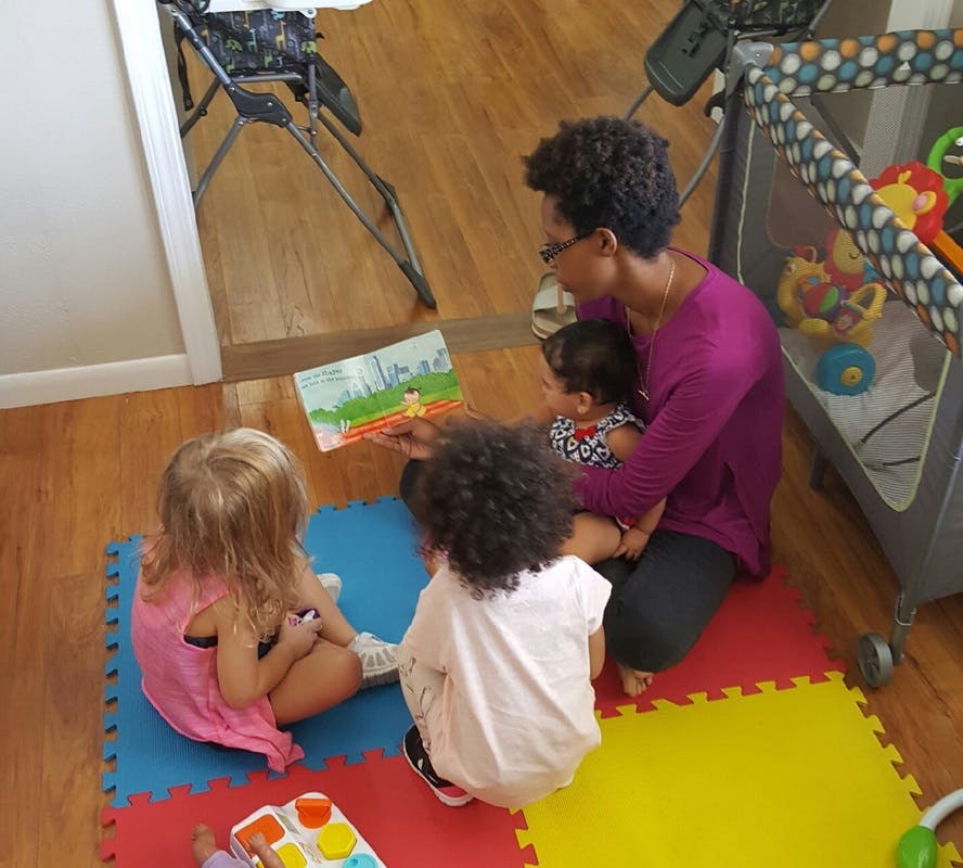 Person reading a book to three children on a colorful mat