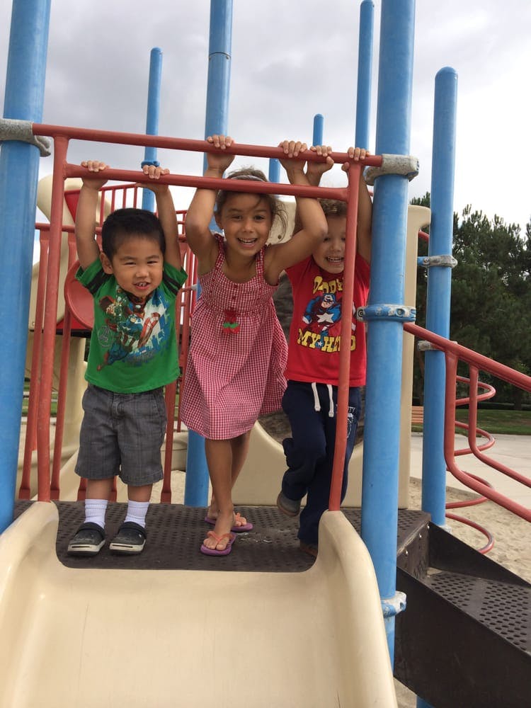 Three children holding onto bars on a playground structure