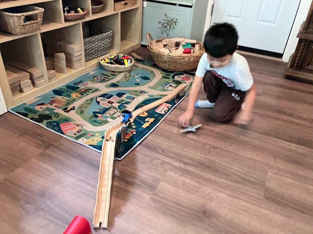 Child playing with a toy airplane on a wooden floor next to a playmat