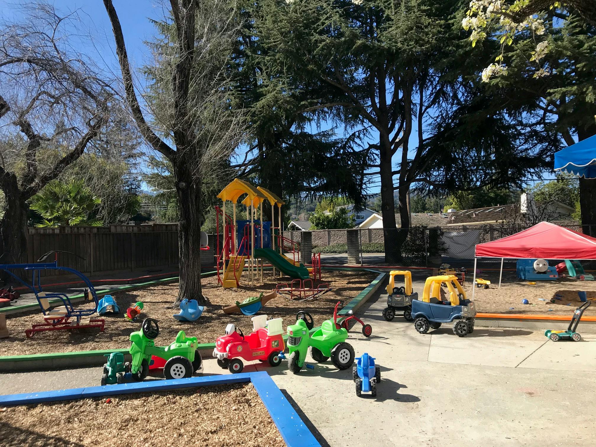 Outdoor playground with play structures, sandbox, and ride-on toys