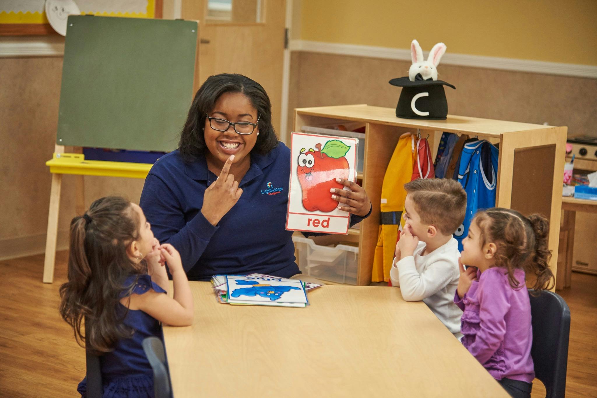 Person holding up a picture of an apple to children in a classroom