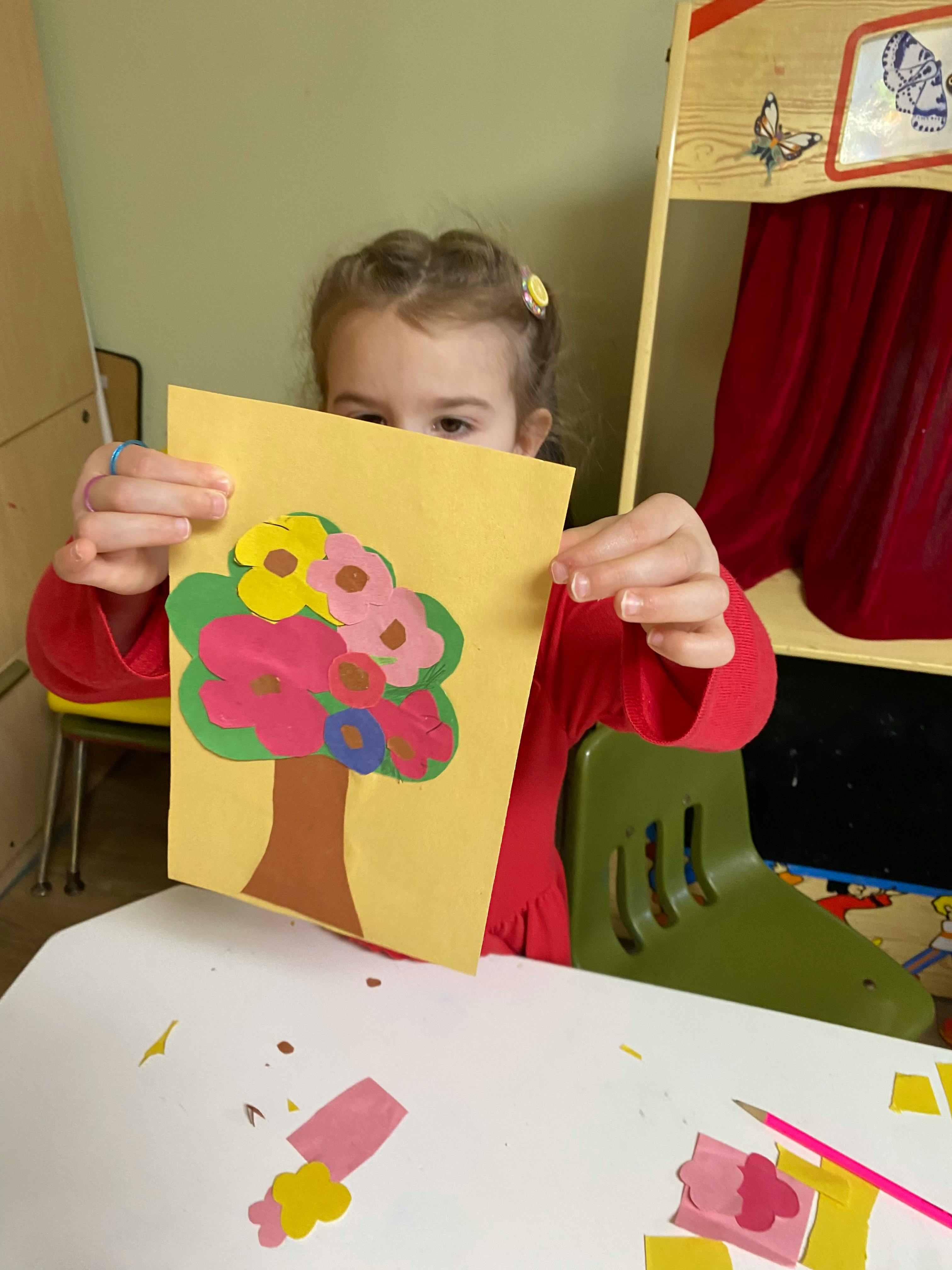 Child holding up a paper craft of a tree with colorful flowers