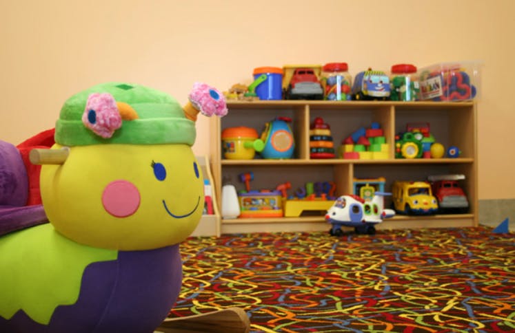 Plush caterpillar toy in a playroom with a shelf of toys