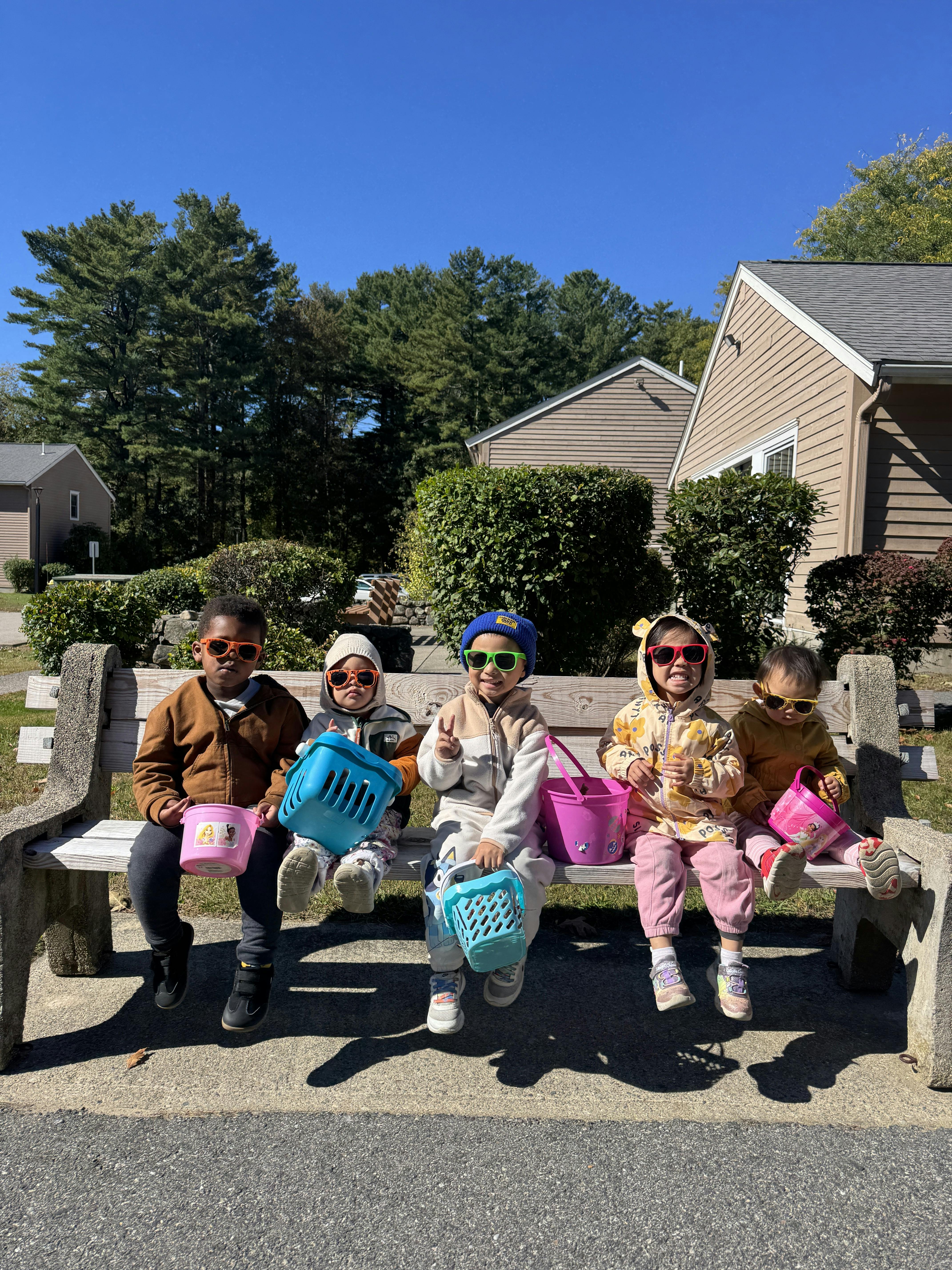 Five children in sunglasses holding small baskets on a park bench