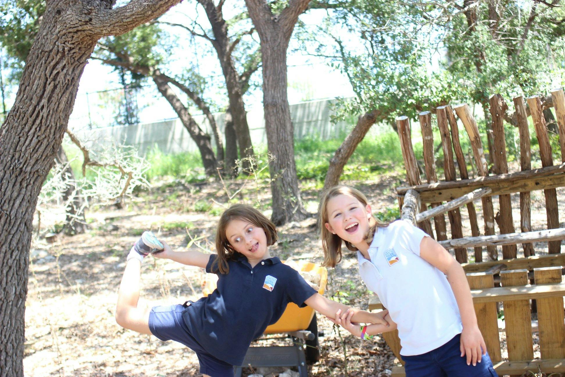 Two children playing outdoors, one balancing on one leg