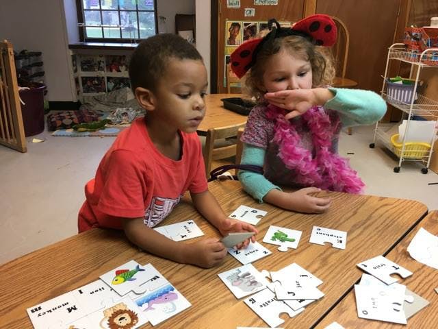 Two children playing with cards at a table in a classroom