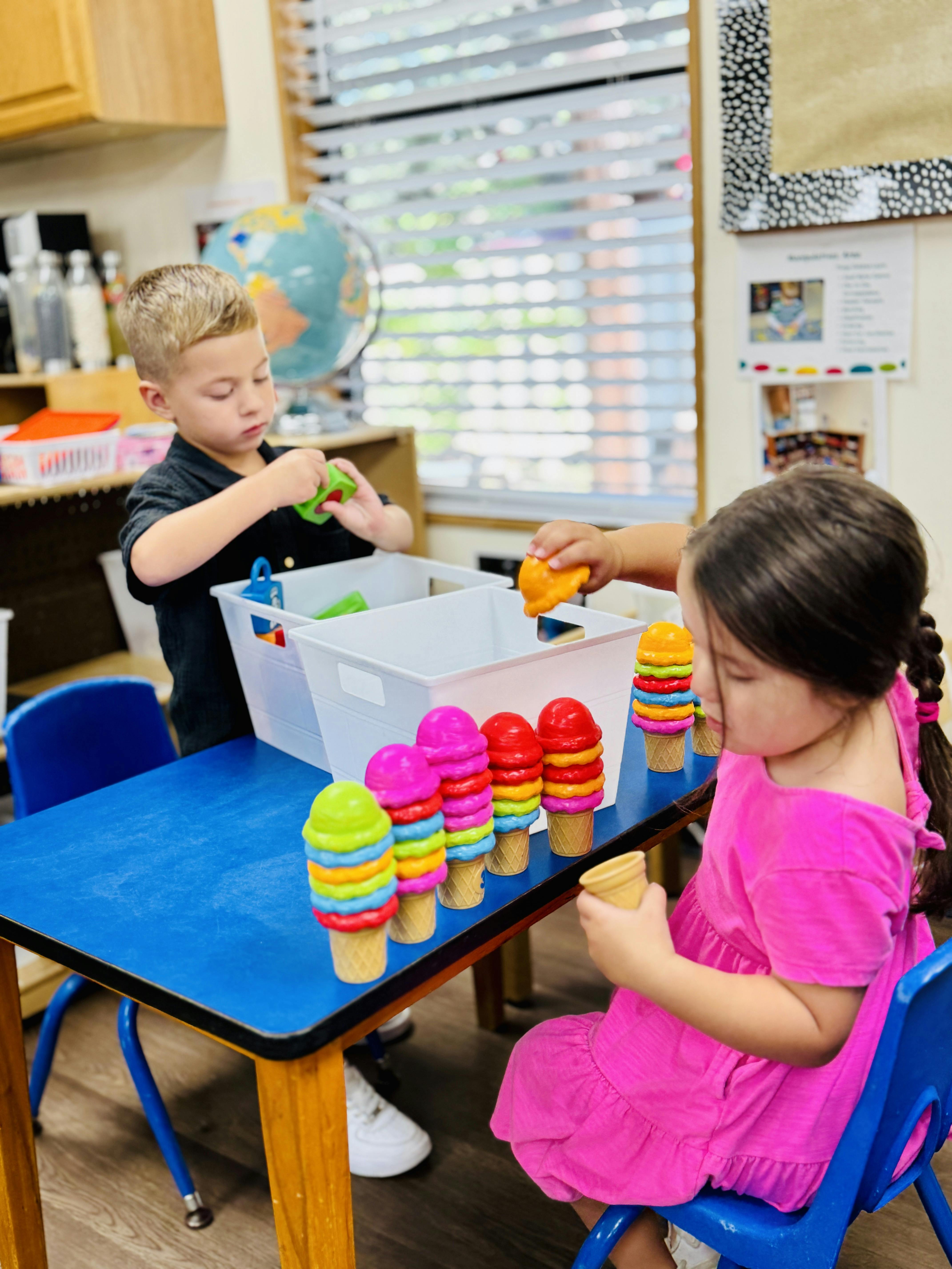 Two children playing with toy ice cream cones at a table in a classroom
