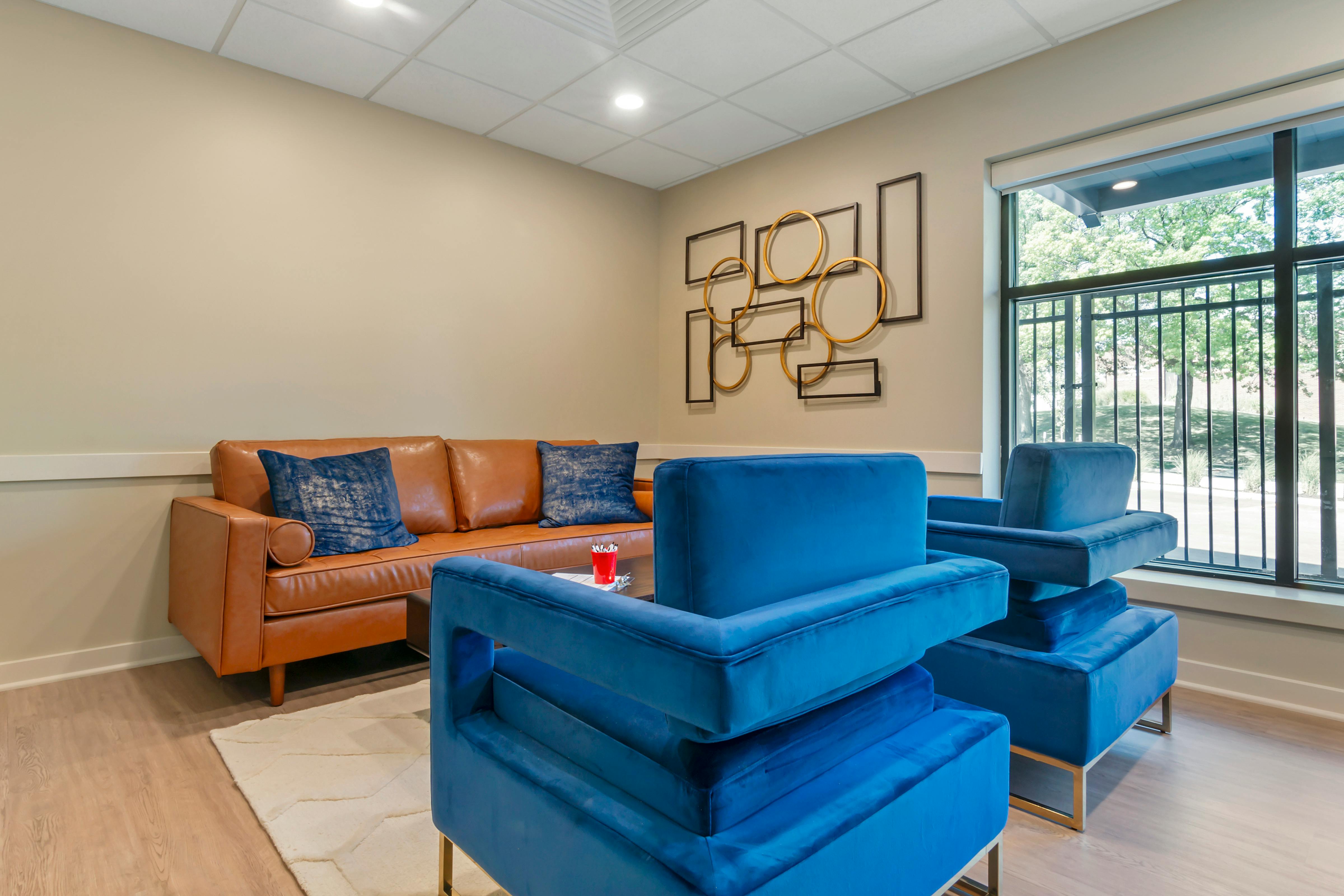 Lounge area with a brown leather sofa, blue velvet chairs, and a window