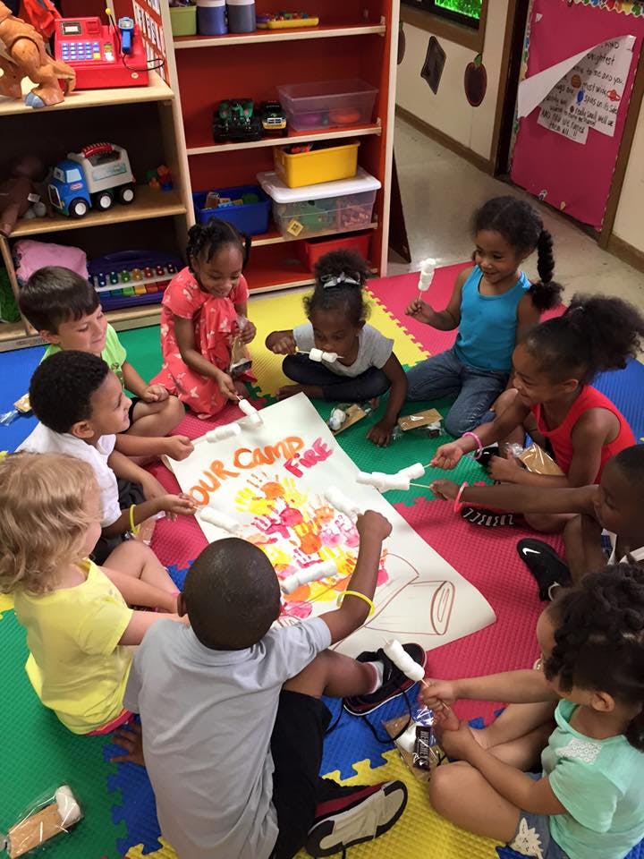 Children sitting on the floor around a banner that says "Our Camp Fire"