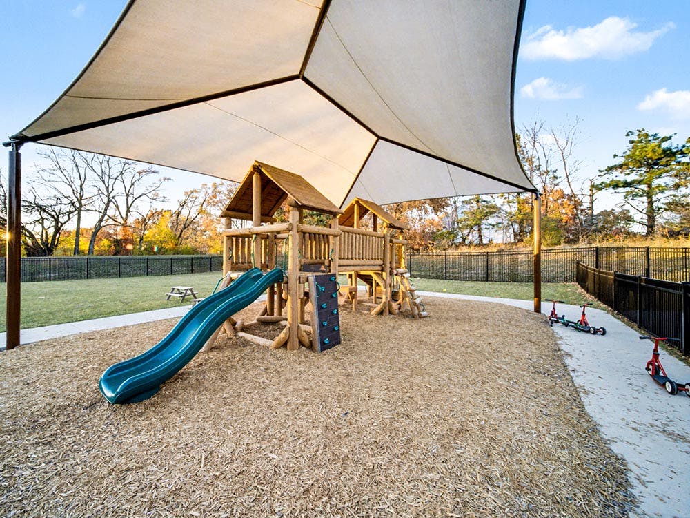 Playground with wooden structure, green slide, and shade sail