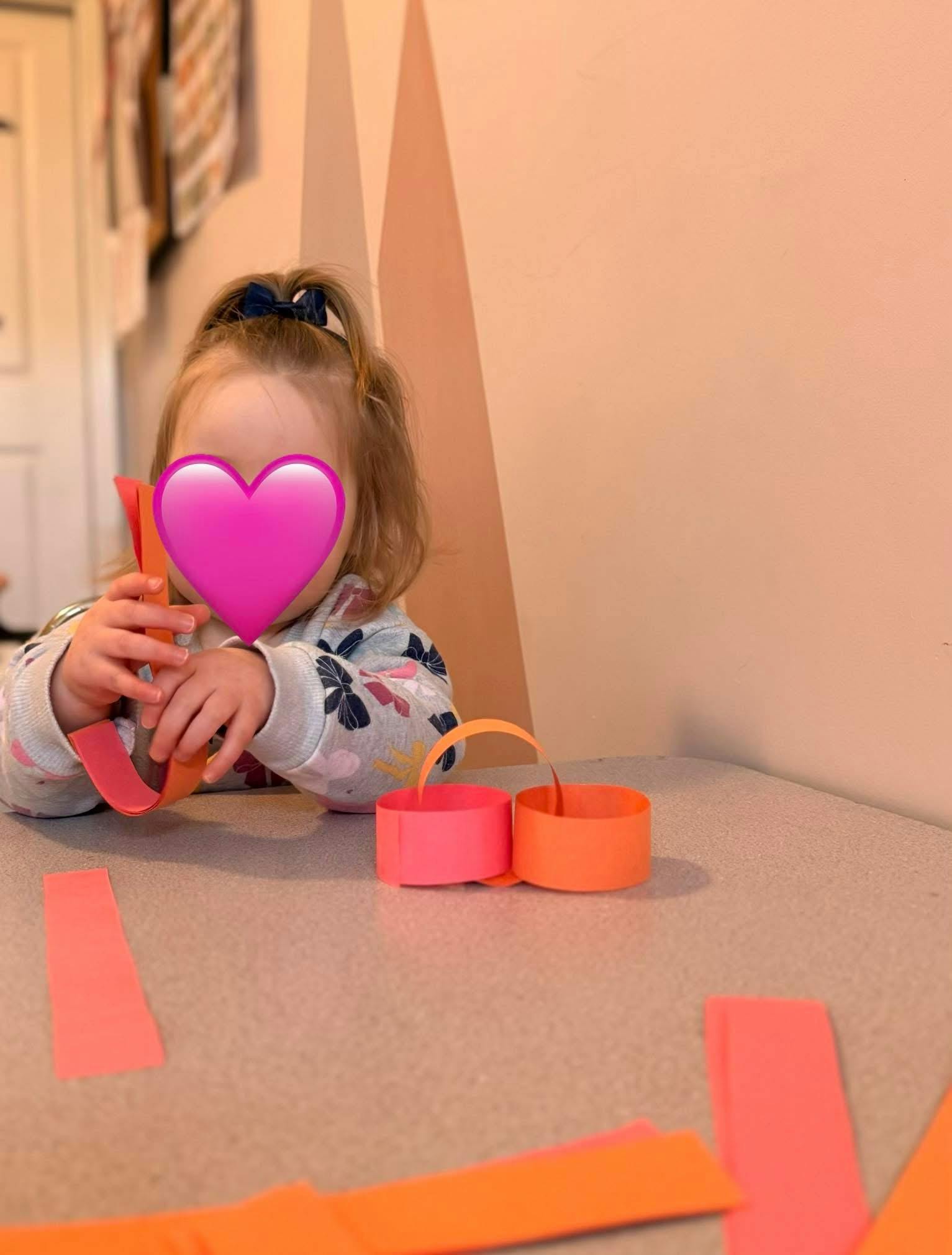 Child holding orange paper strips, with more strips on a table