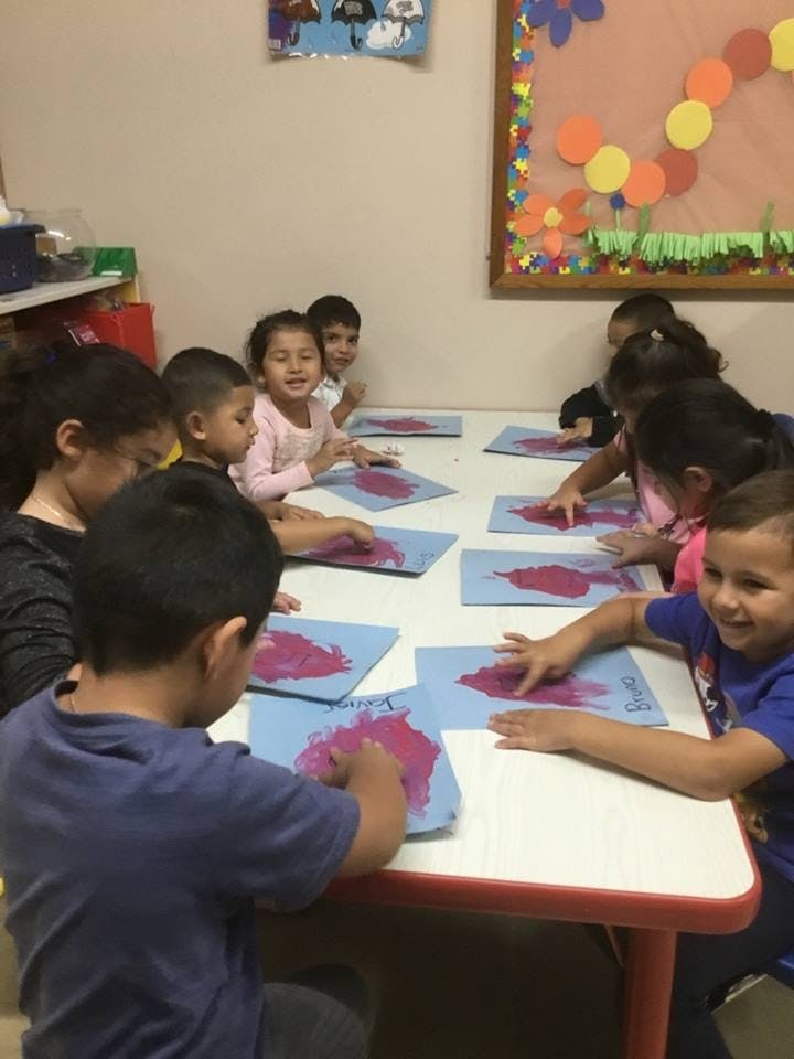 Children sitting at a table doing an art activity with red paint