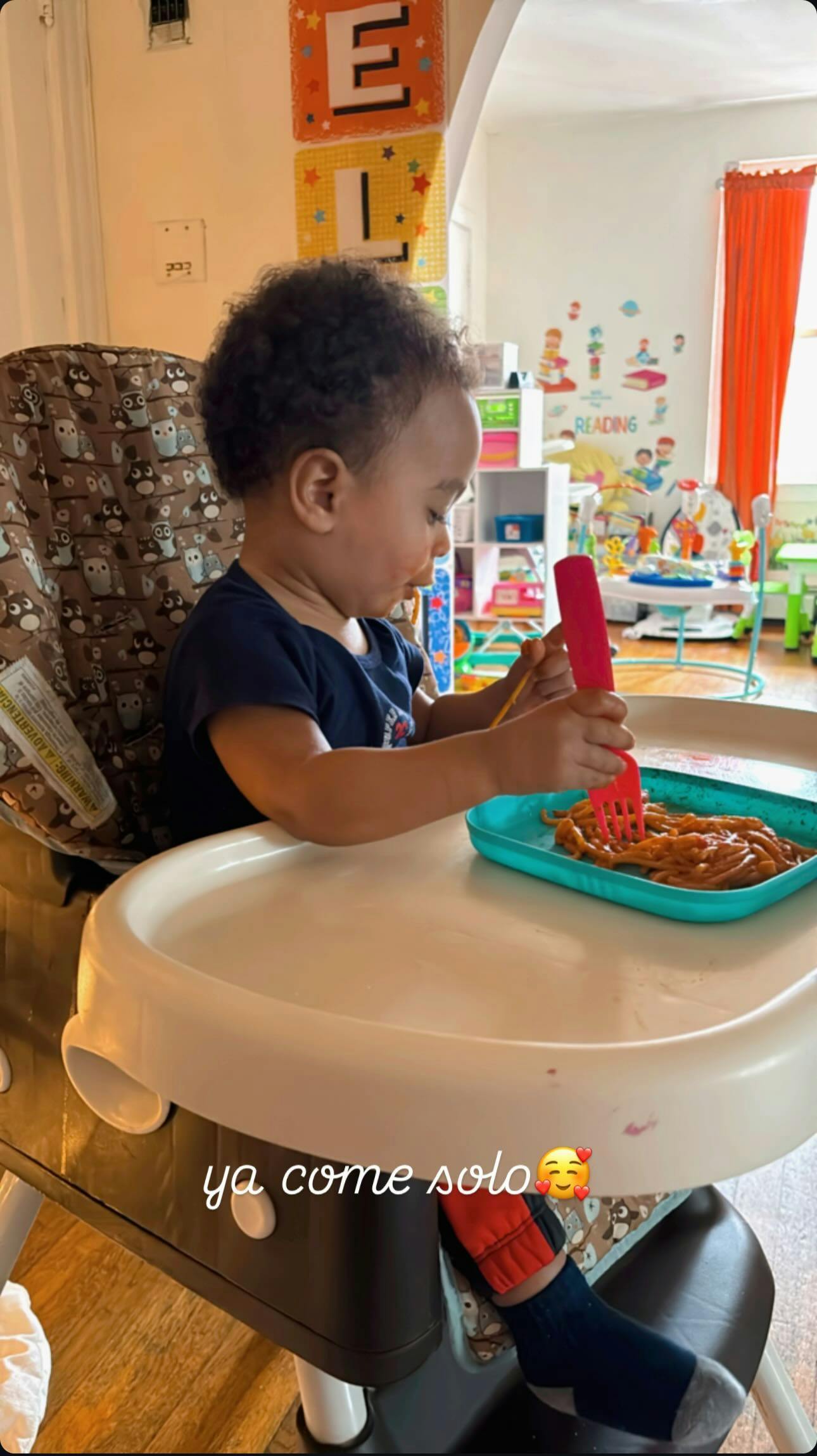Child in a high chair eating pasta with a fork
