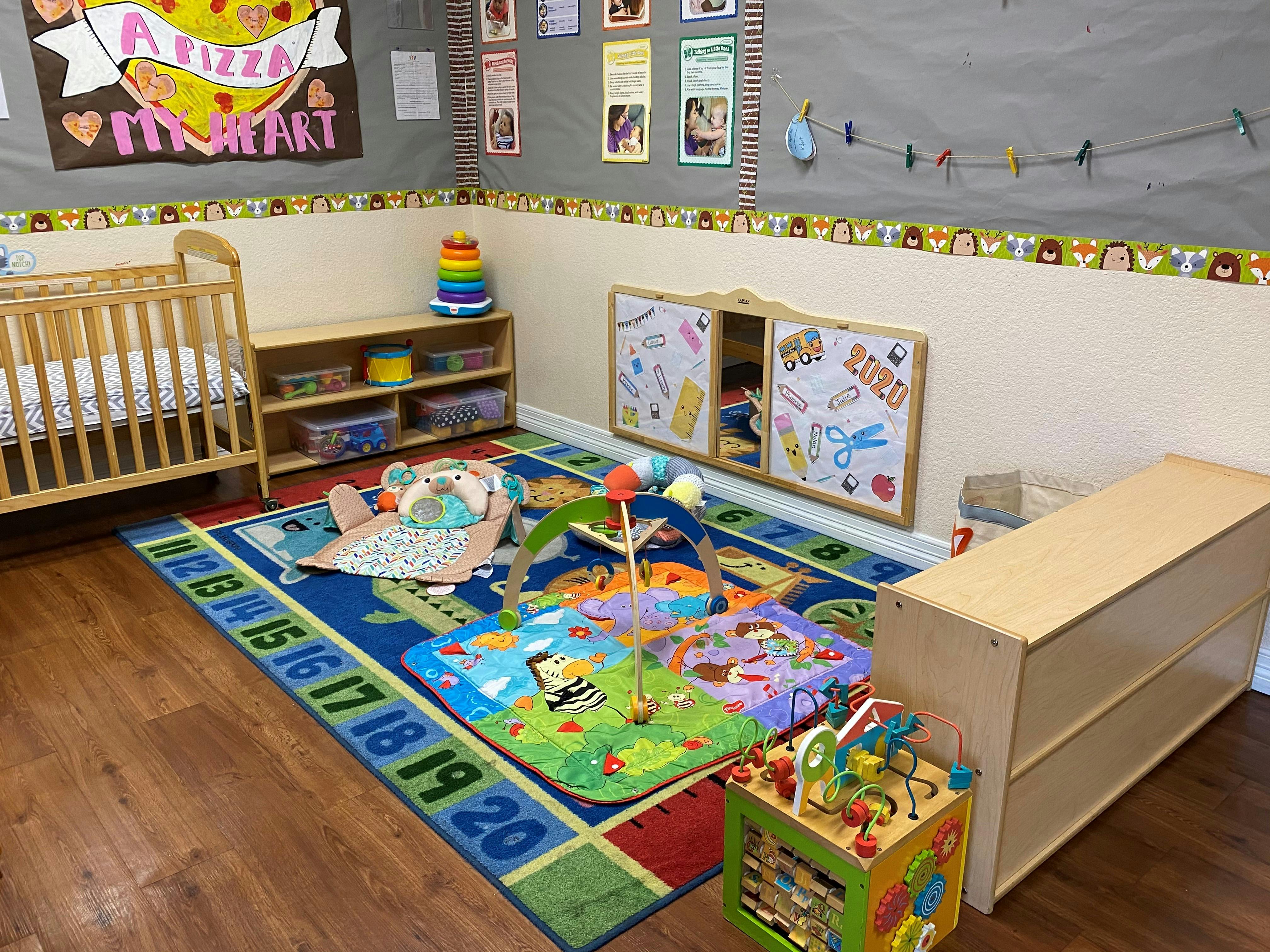 Nursery room with a crib, playmats, and toys on the wall a sign that says "A Pizza My Heart"