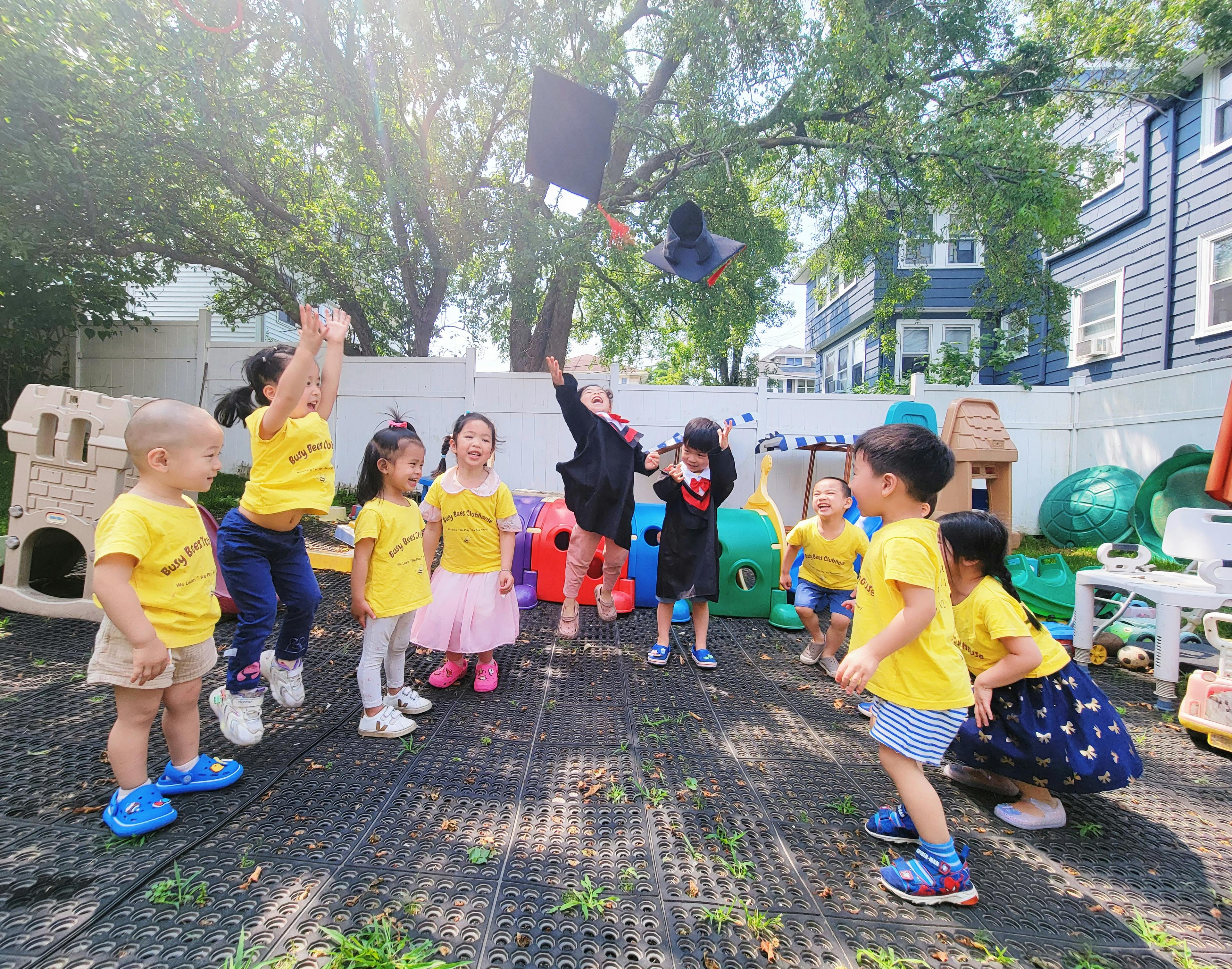 Children in yellow shirts and one in a graduation gown throwing a cap in the air