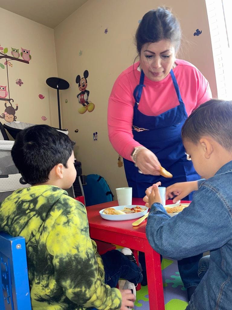 Adult serving food to two children at a table