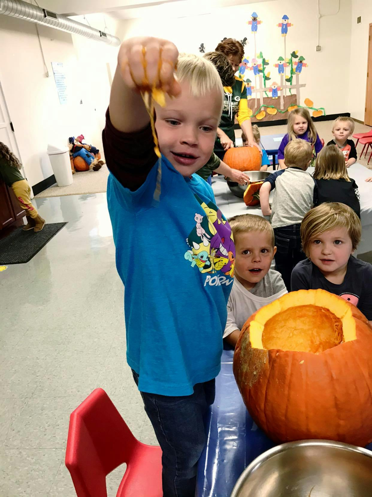 Child holding up pumpkin guts with other children and pumpkins in a classroom