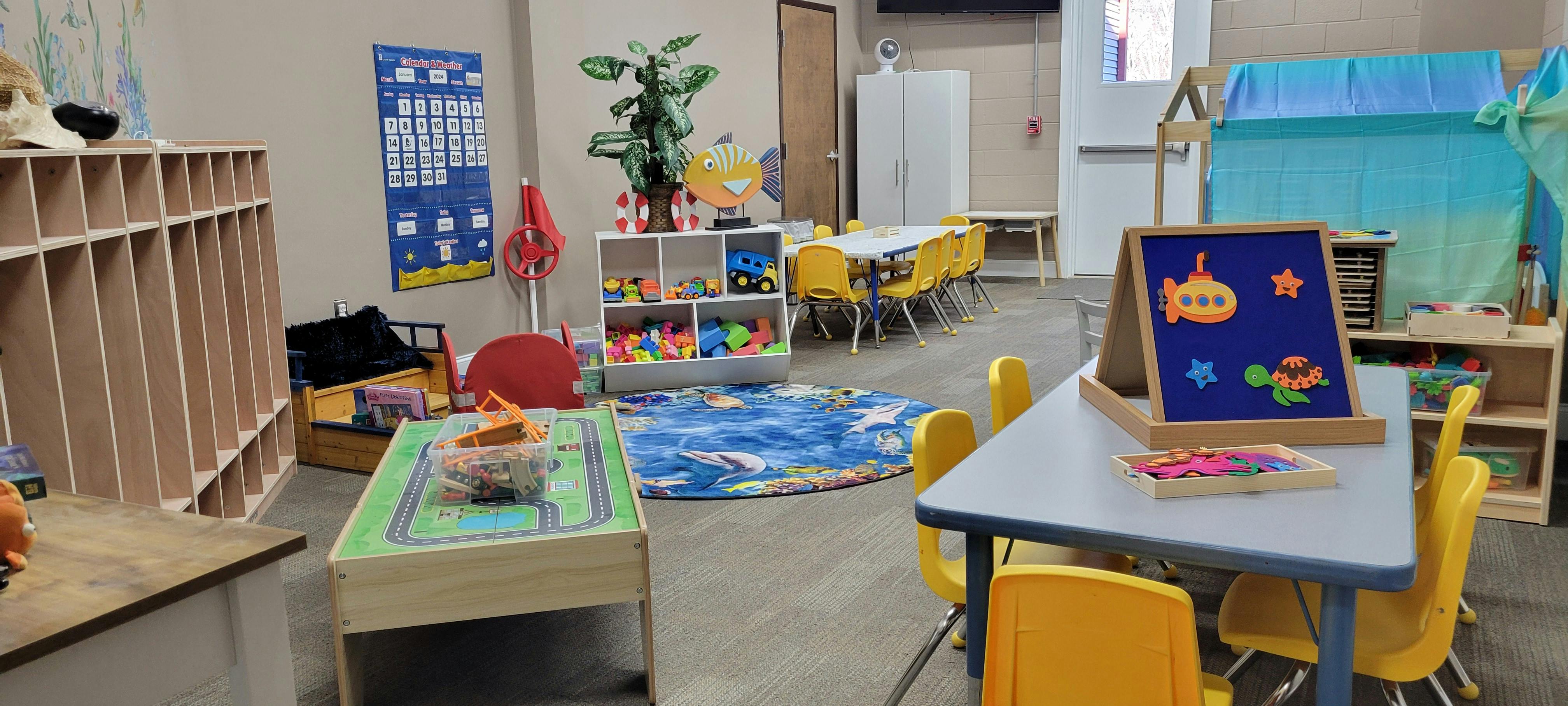 Classroom filled with child-sized tables and chairs, shelves, toys, and a calendar