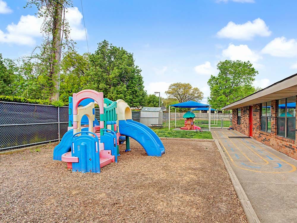Colorful playground structure on wood chips next to a brick building