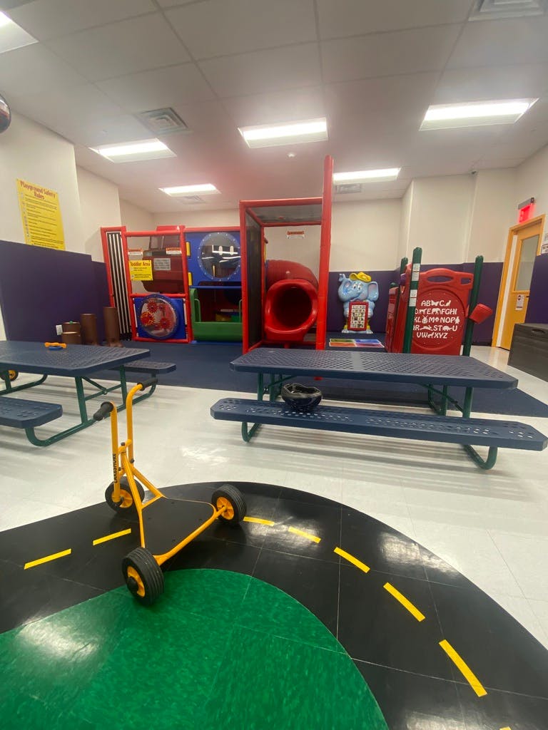 Indoor playground with slides, tunnels, picnic tables, and a ride-on toy