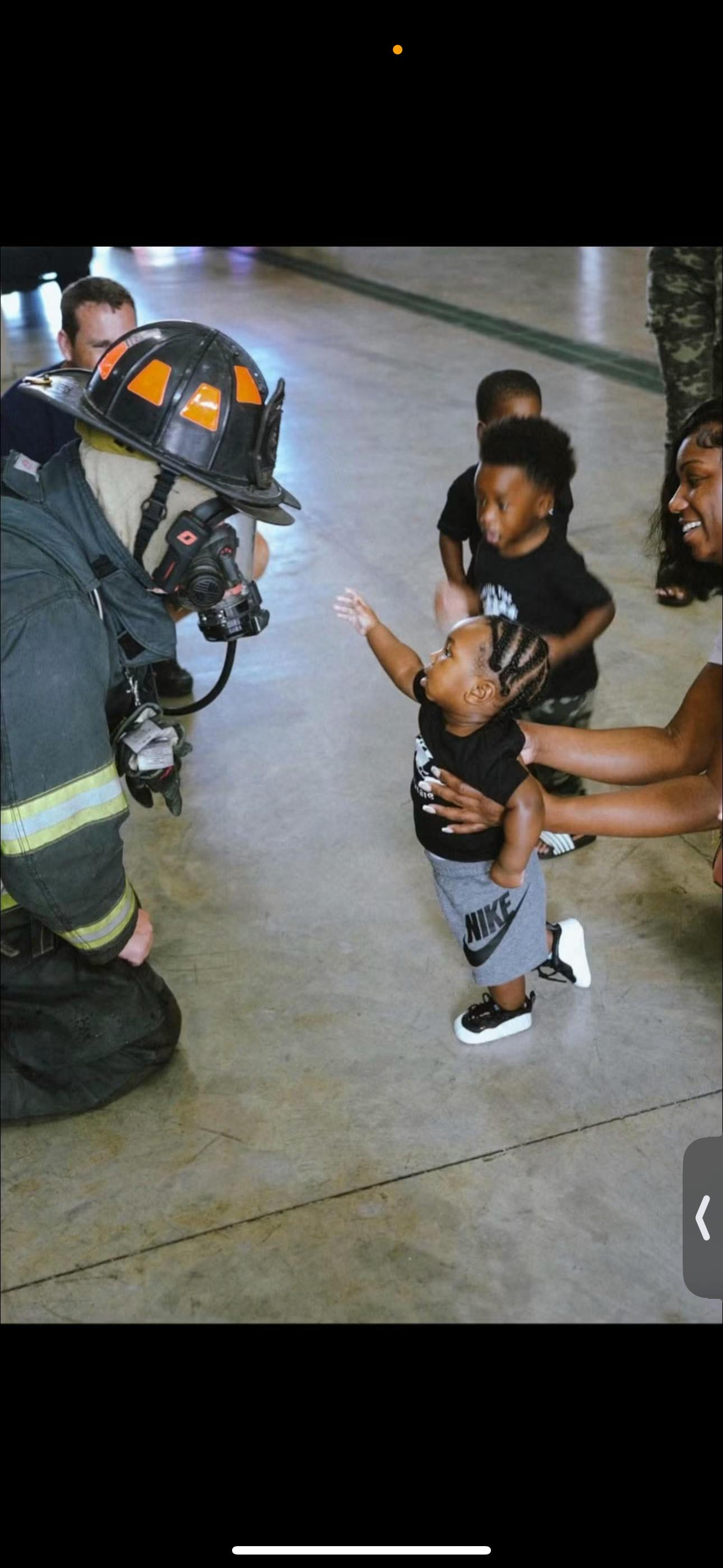 A small child reaching toward a firefighter in full gear