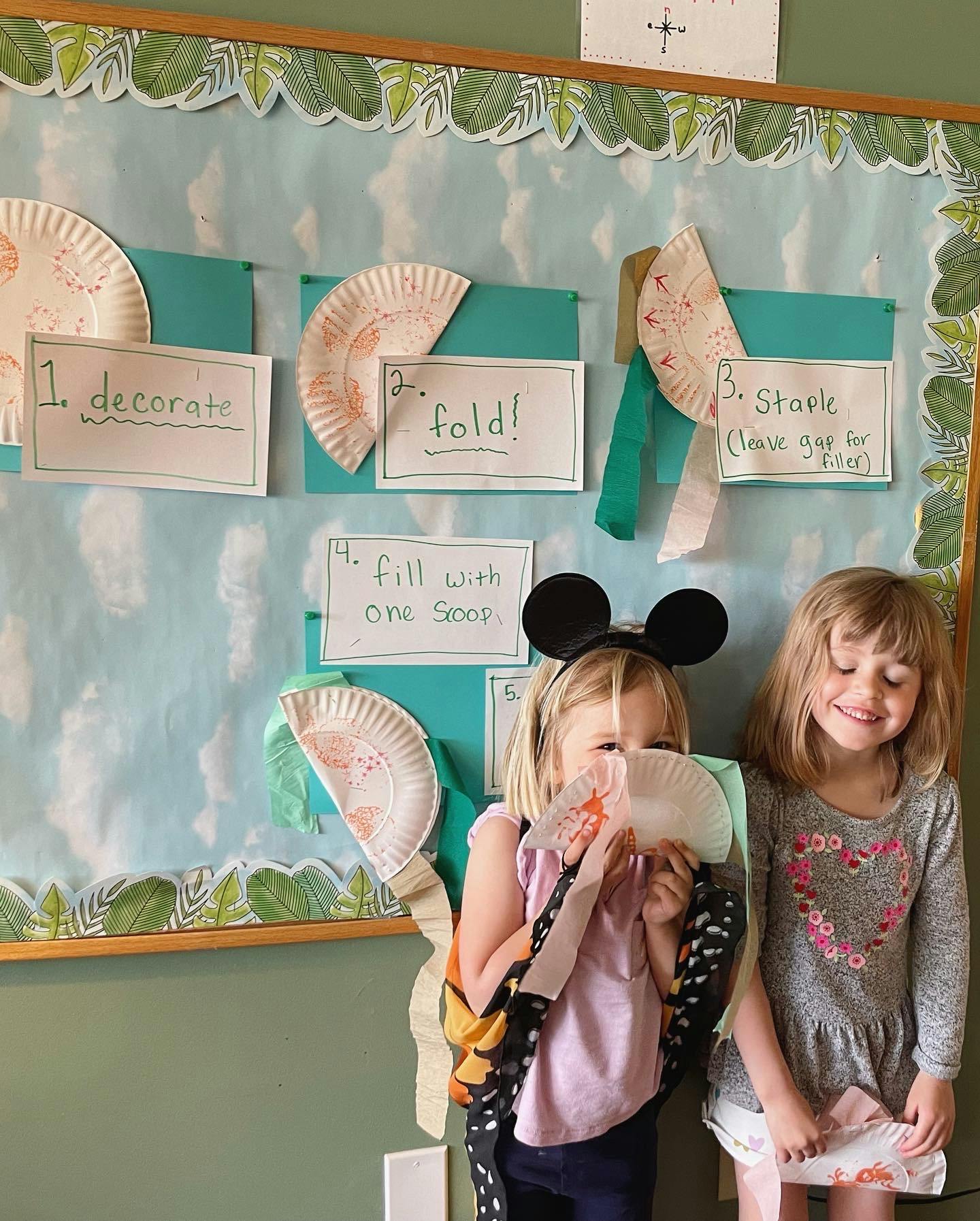 Two children standing in front of a bulletin board with craft instructions