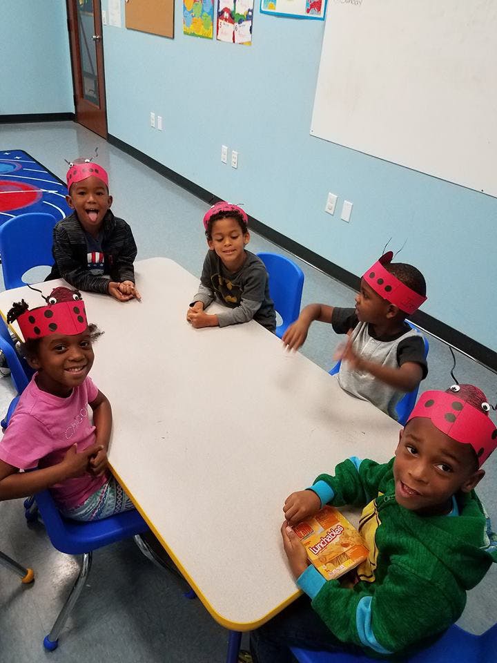 Five children wearing red headbands sitting at a table in a classroom