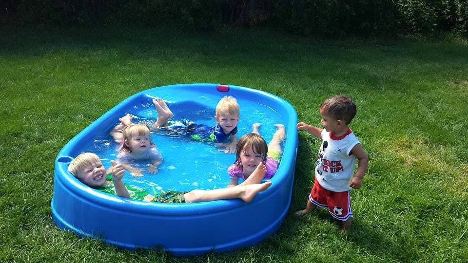 Children playing in a small blue wading pool on grass