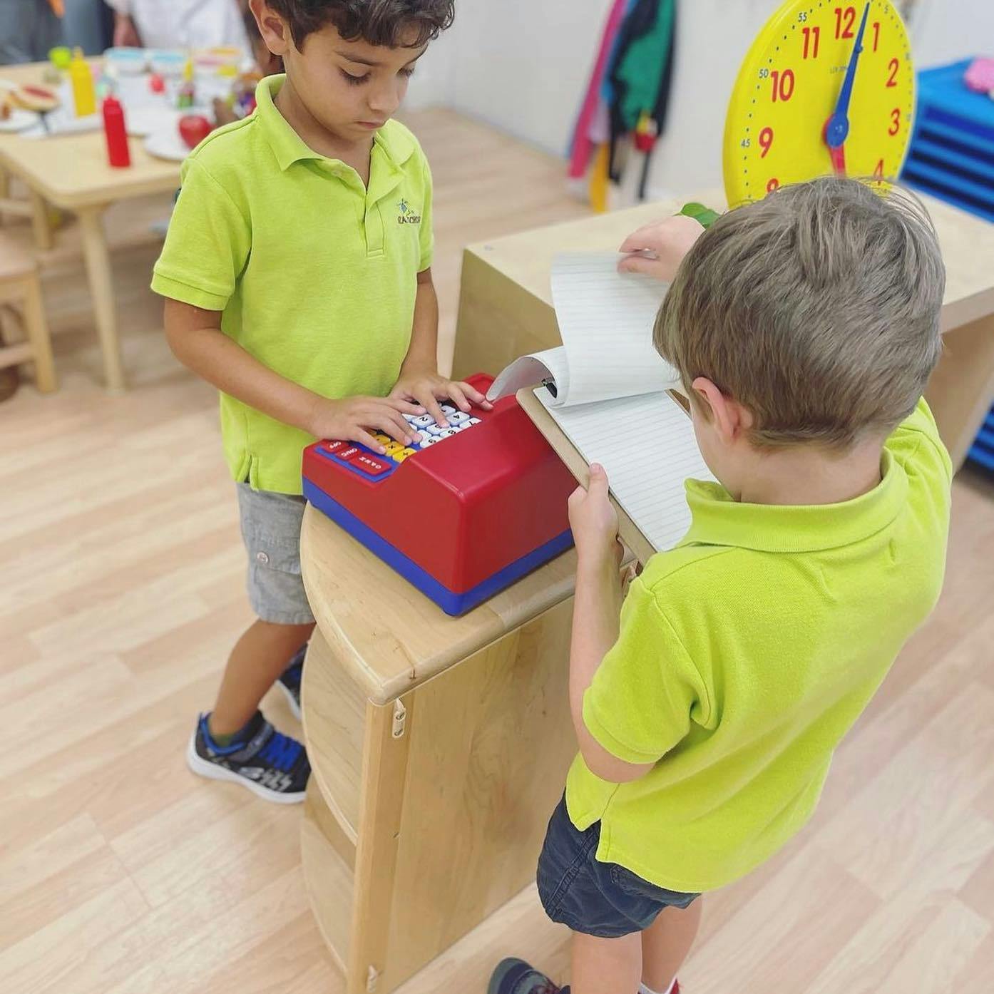 Two children playing with a toy cash register and a notebook