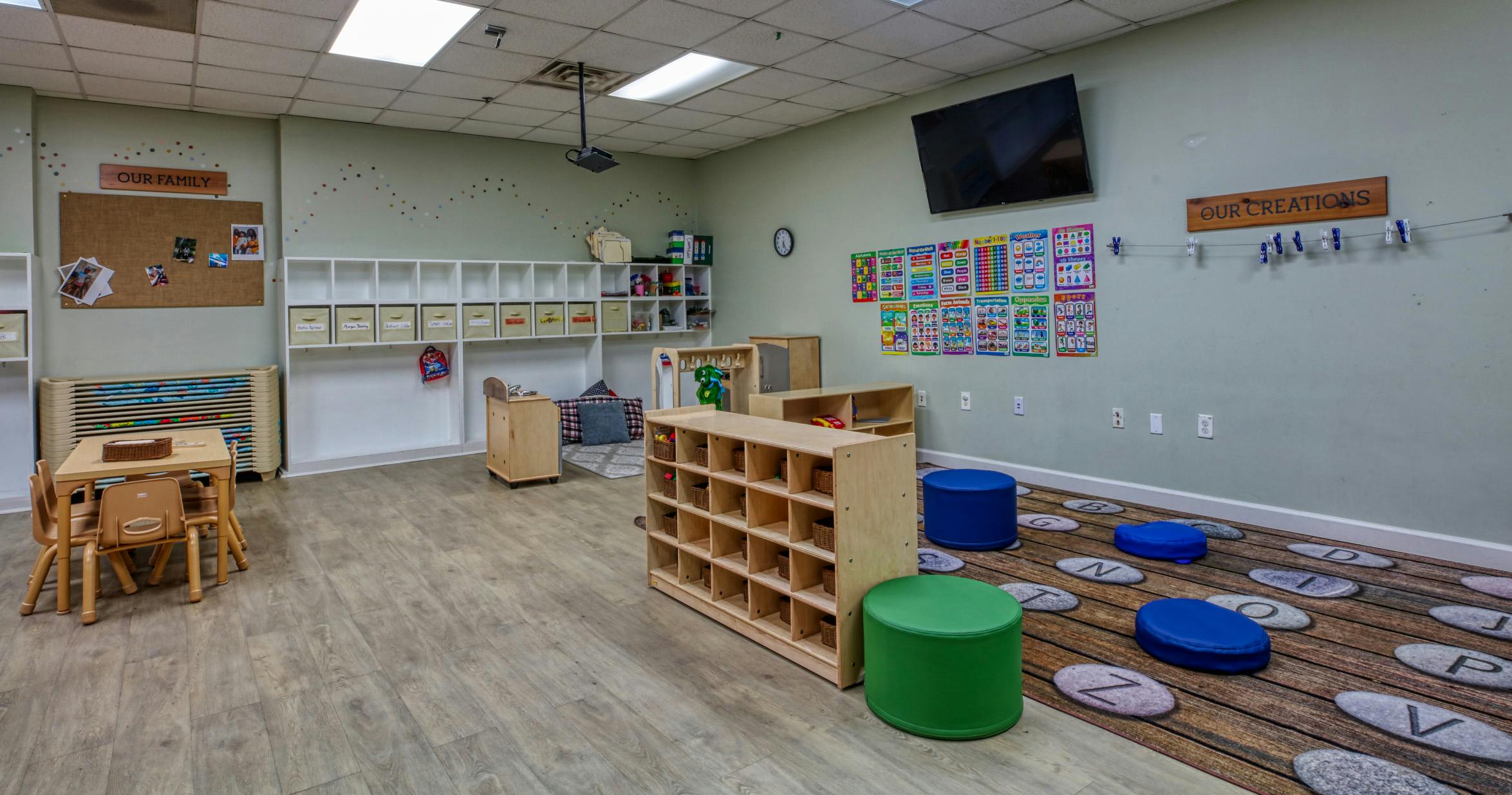 Classroom with child-sized furniture, shelves, educational posters, and alphabet rug