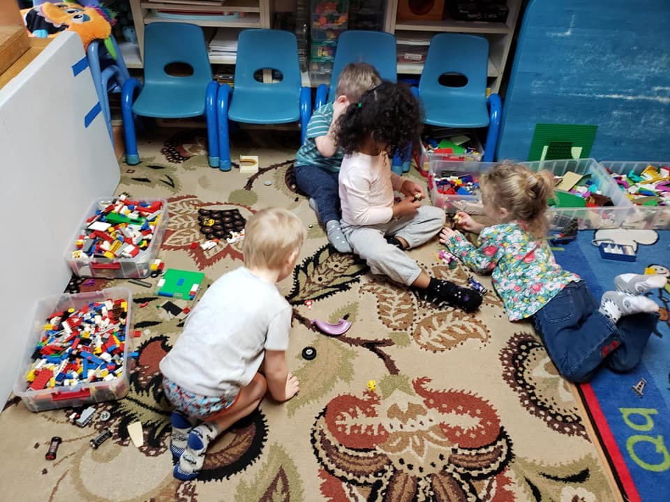 Four children playing with building blocks on a patterned rug