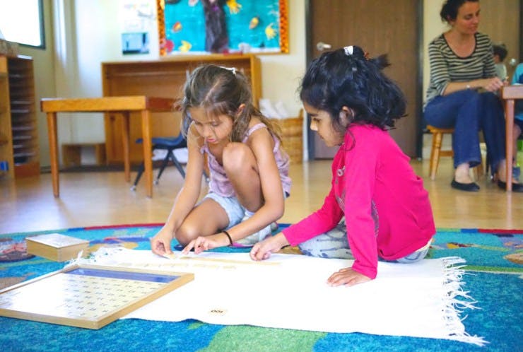 Two children sitting on a rug and working with learning materials