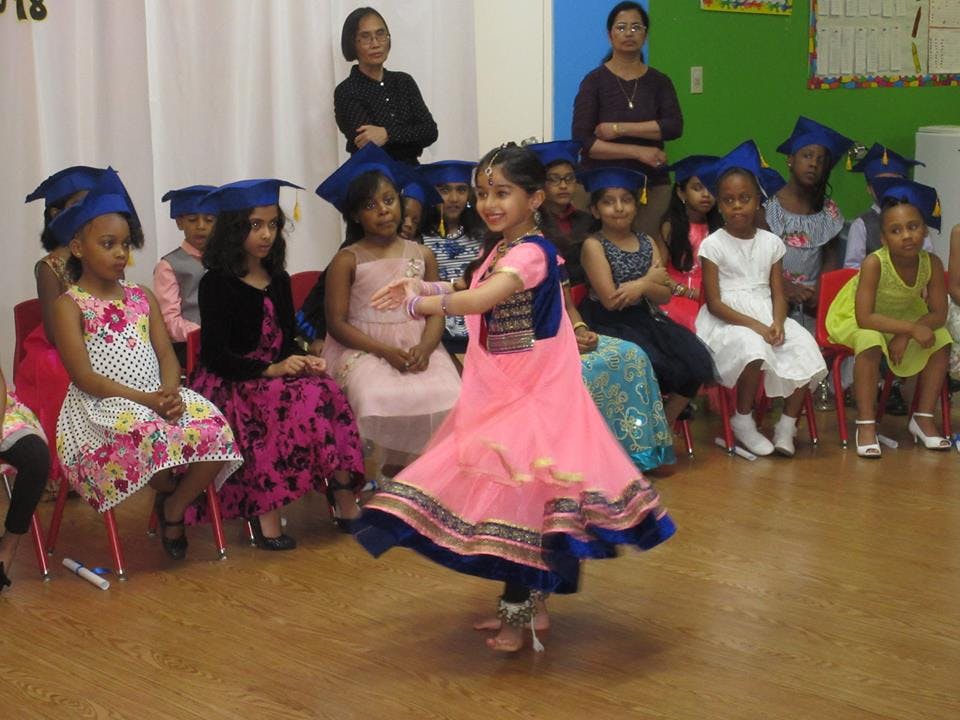Child in pink dress dancing in front of seated children in graduation caps