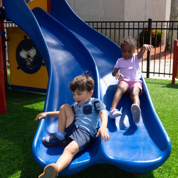 Two children sliding down a blue playground slide