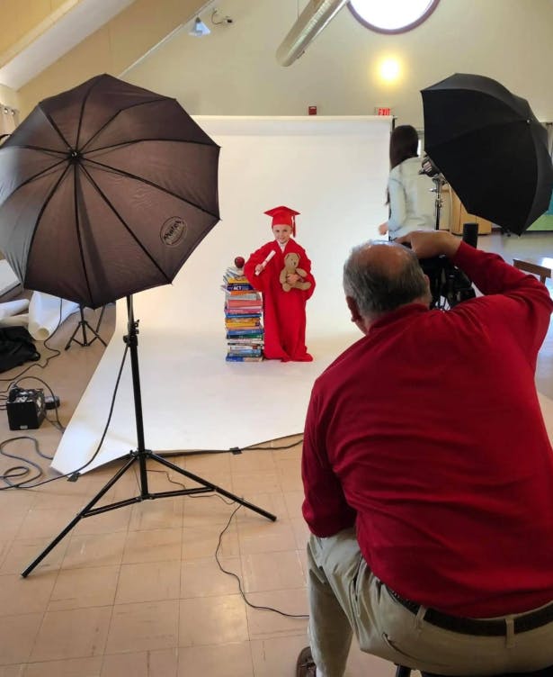 Person in red graduation gown and cap holding a teddy bear, being photographed
