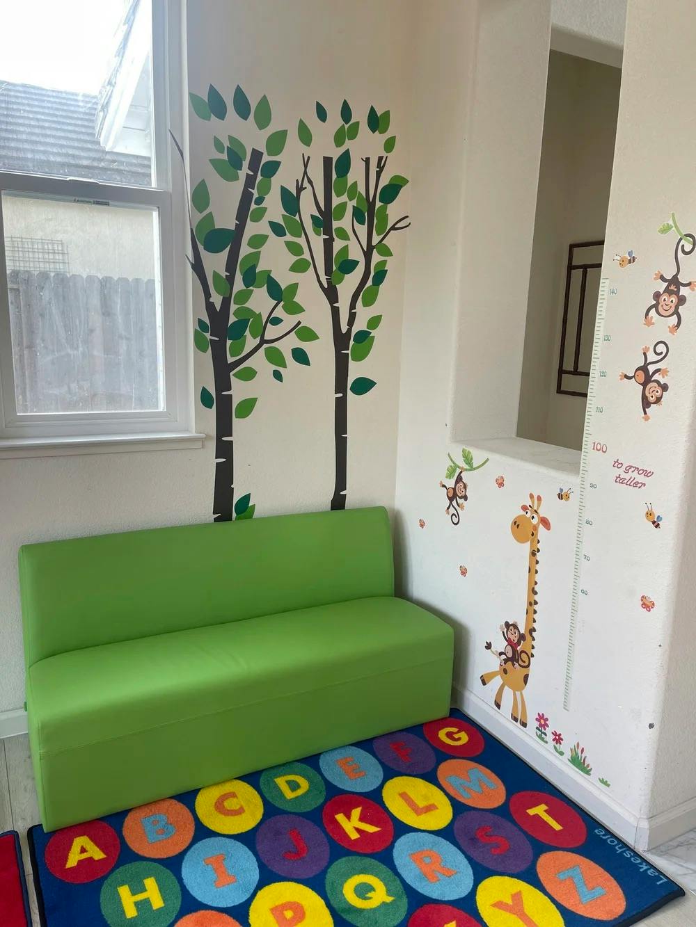 Green bench and alphabet rug in a playroom with wall decals of trees and animals