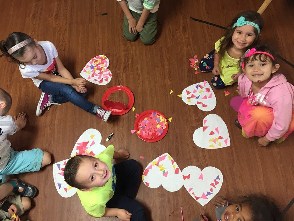 Children sitting on floor making heart-shaped crafts