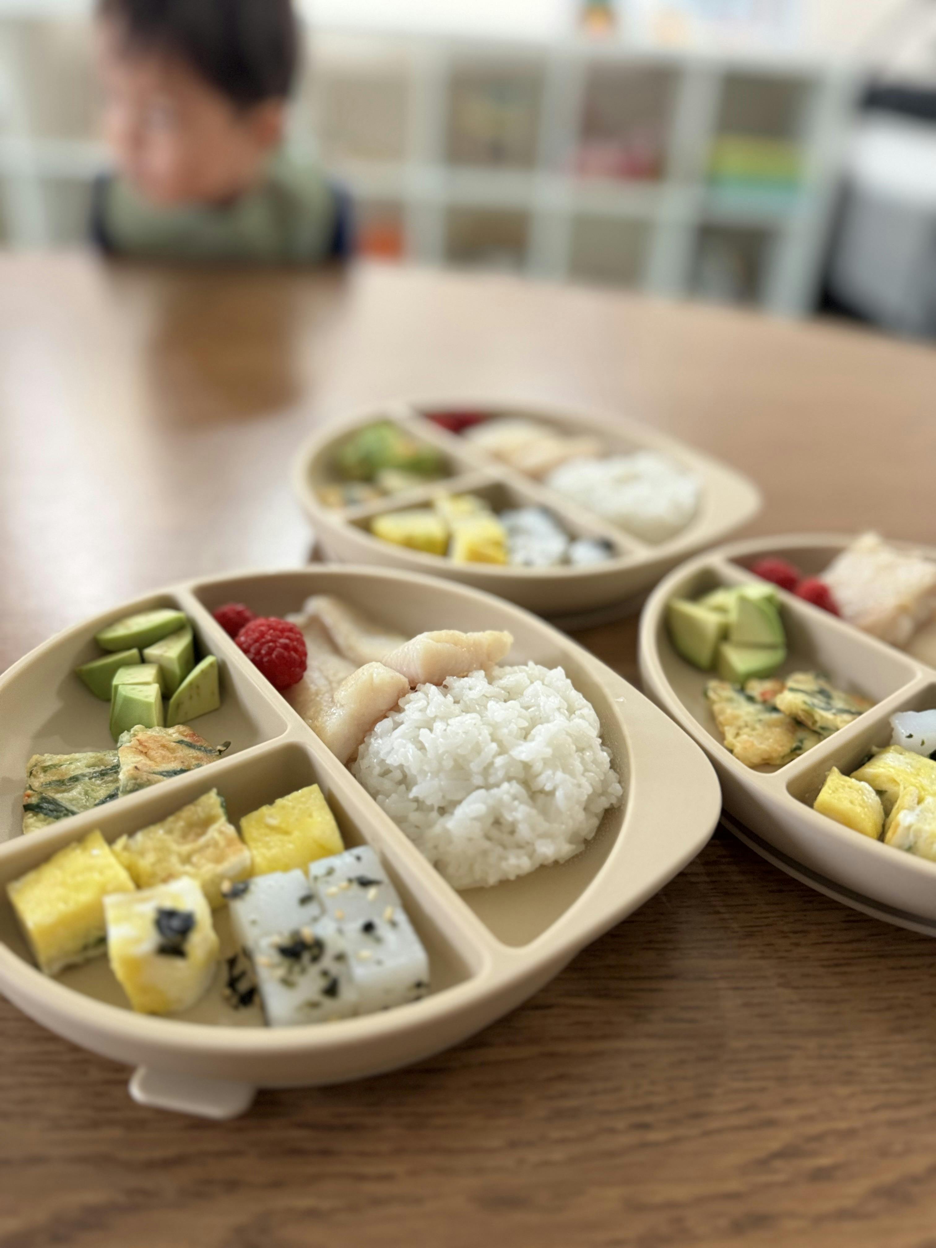 Several plates of food on a table, including rice, fish, avocado, and raspberries
