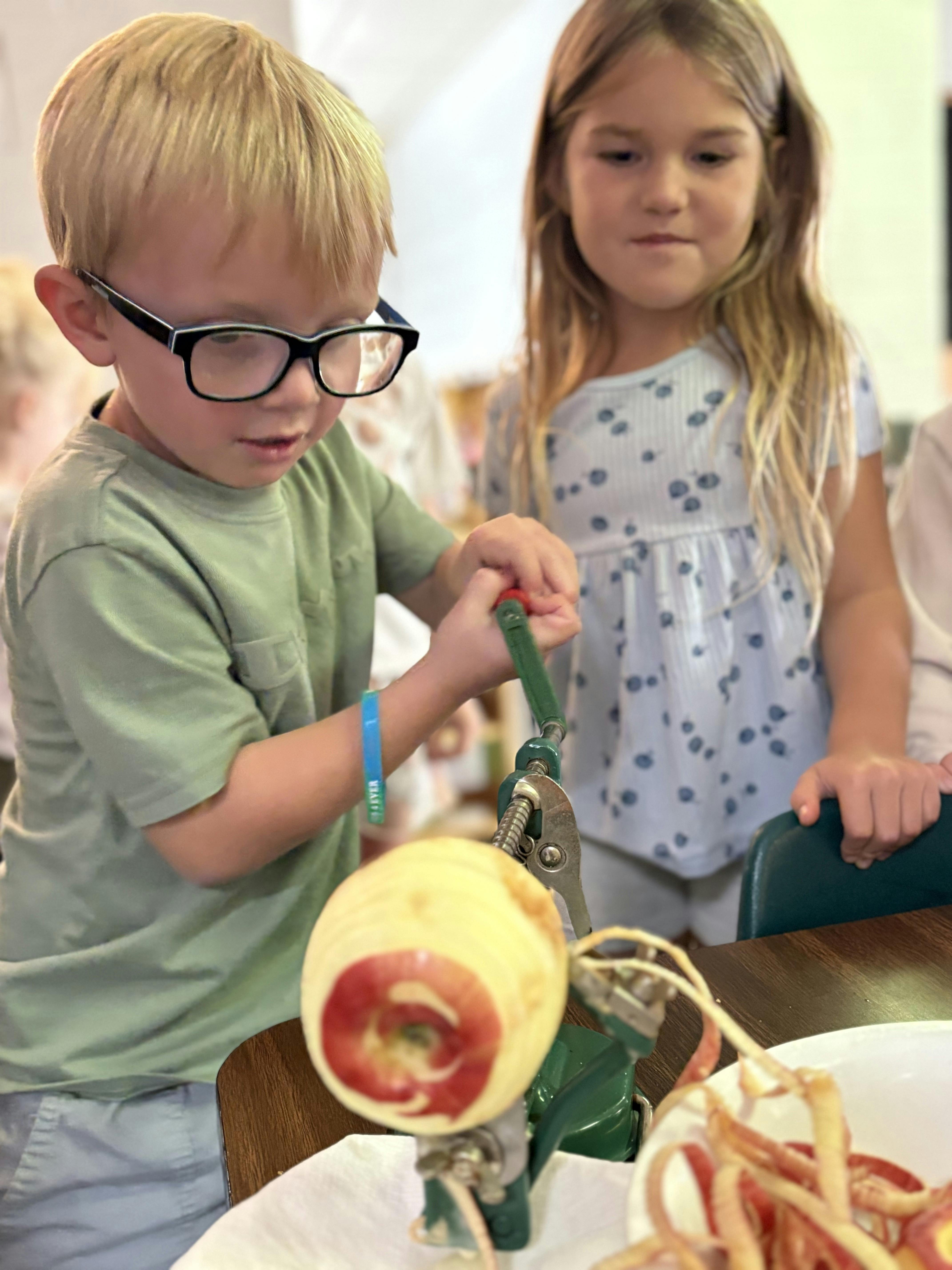 Child peeling an apple with a peeler, another child watching