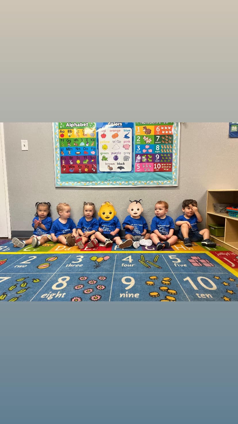 Six children sitting on a numbered mat in front of an alphabet chart