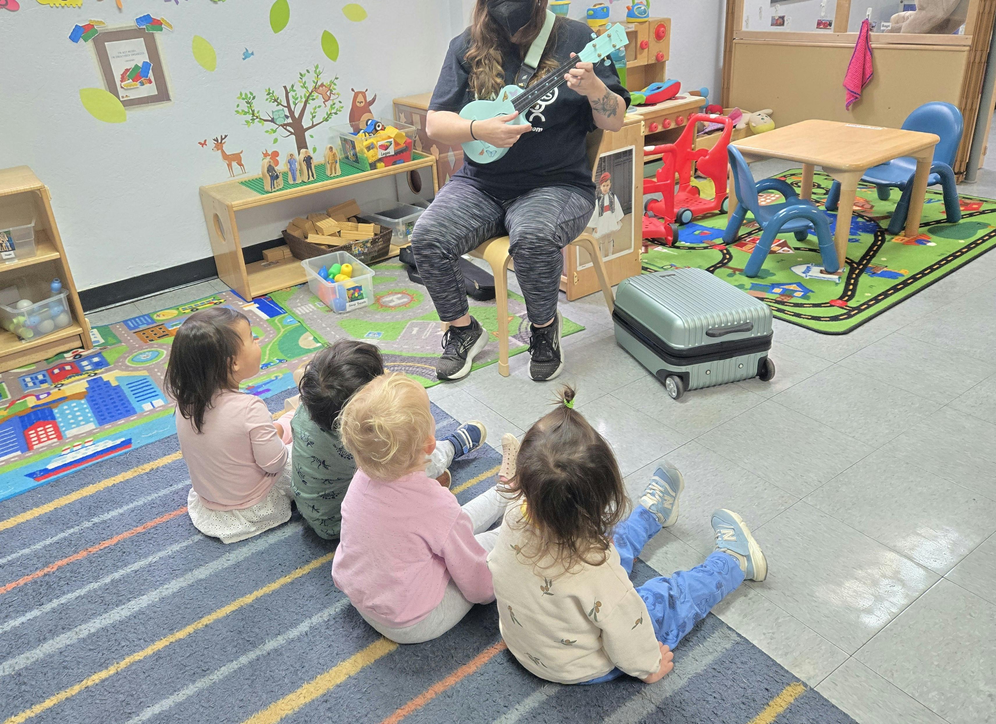 Person playing ukulele for children sitting on floor