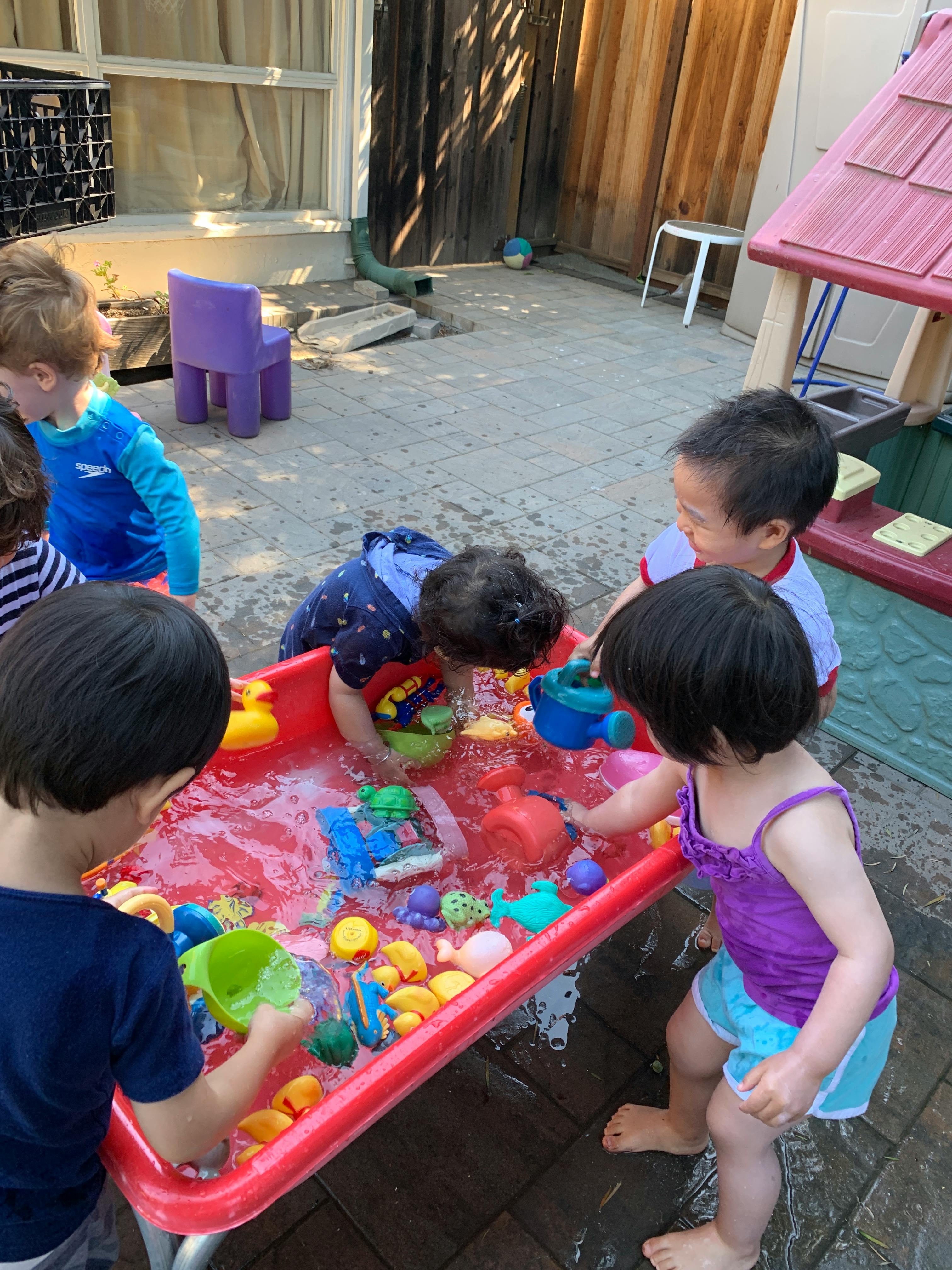 Children playing with water and toys in a red water table