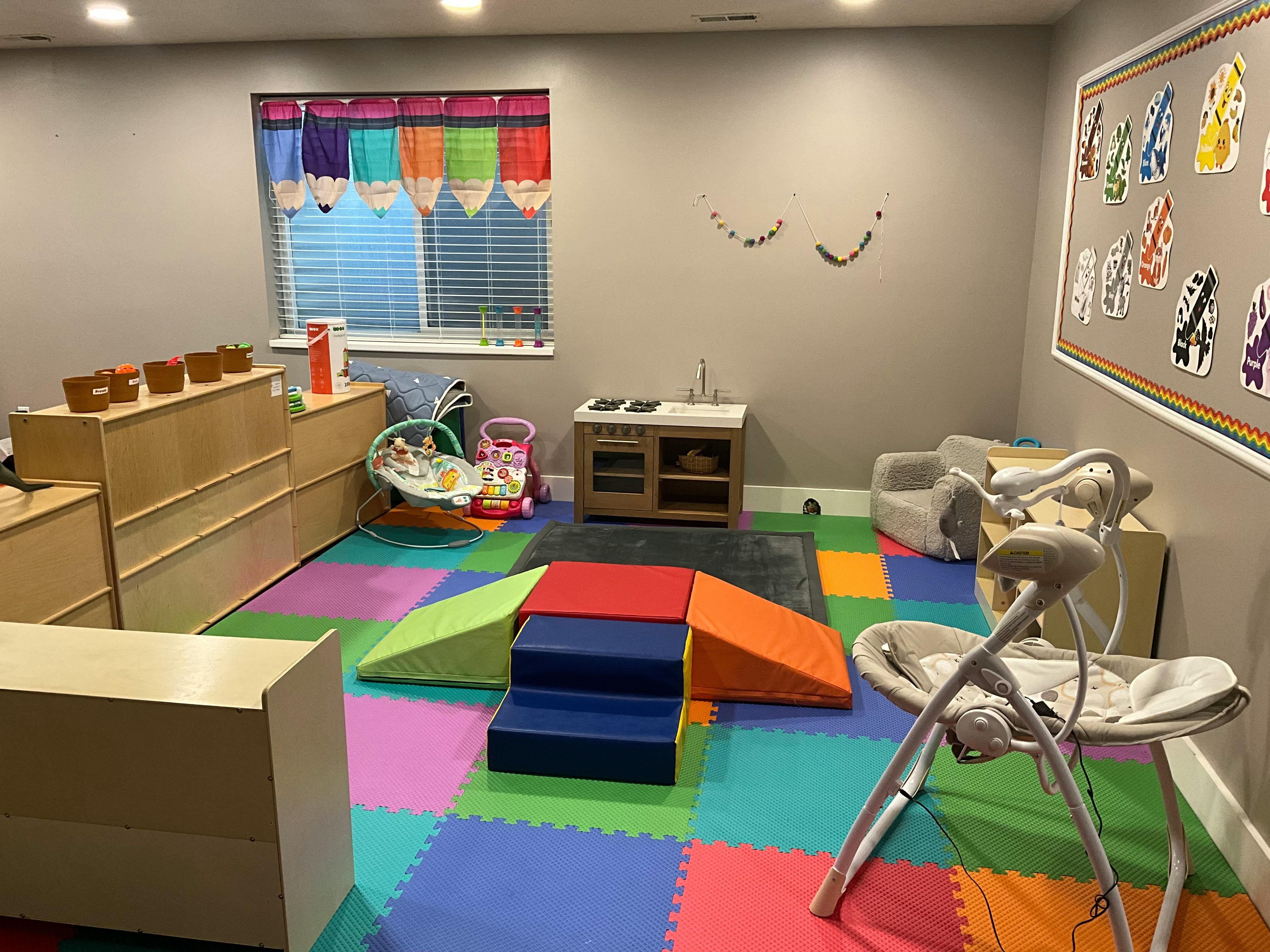 Indoor play area with colorful floor mats, soft play equipment, and baby swing