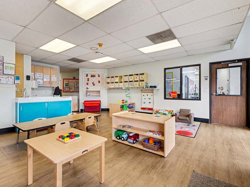 Classroom with child-sized tables, chairs, a sink, and toy storage shelves