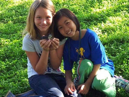 Two children sitting in grass, one holding a small object