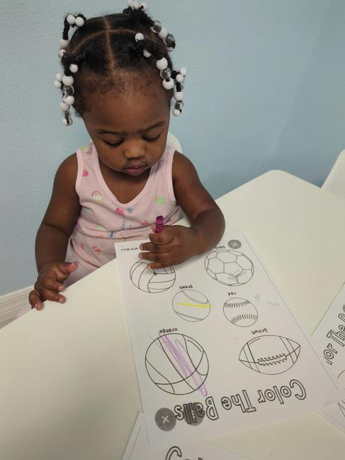 Child coloring on a worksheet featuring illustrations of various sports balls