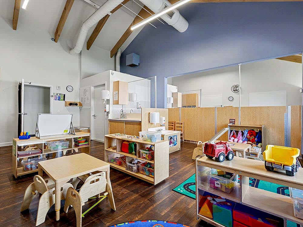 Classroom with small wooden tables and chairs, toys, and whiteboards