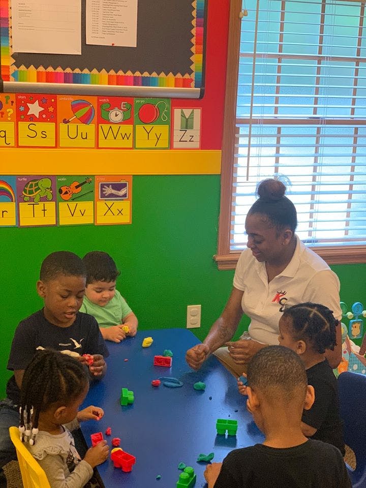 Adult and children playing with toys at a table in a classroom