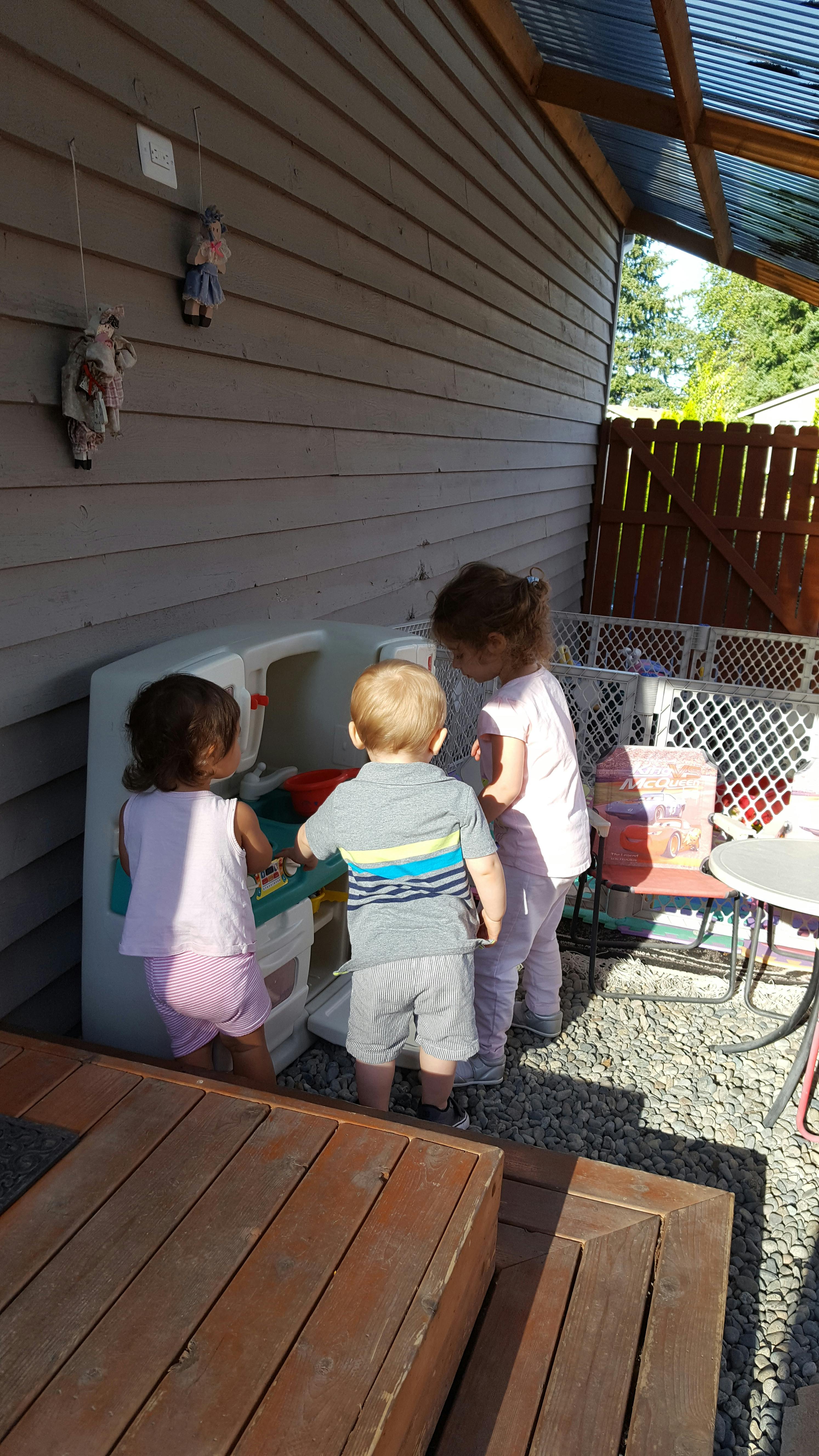 Three children playing with a toy kitchen in an outdoor setting